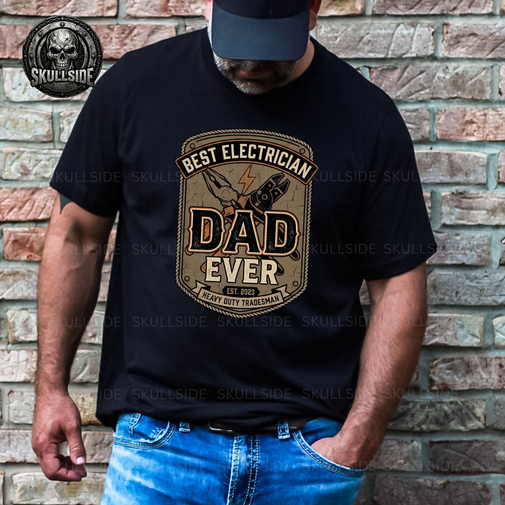Man wearing a black t-shirt with 'Best Electrician Dad Ever' design against a brick wall.